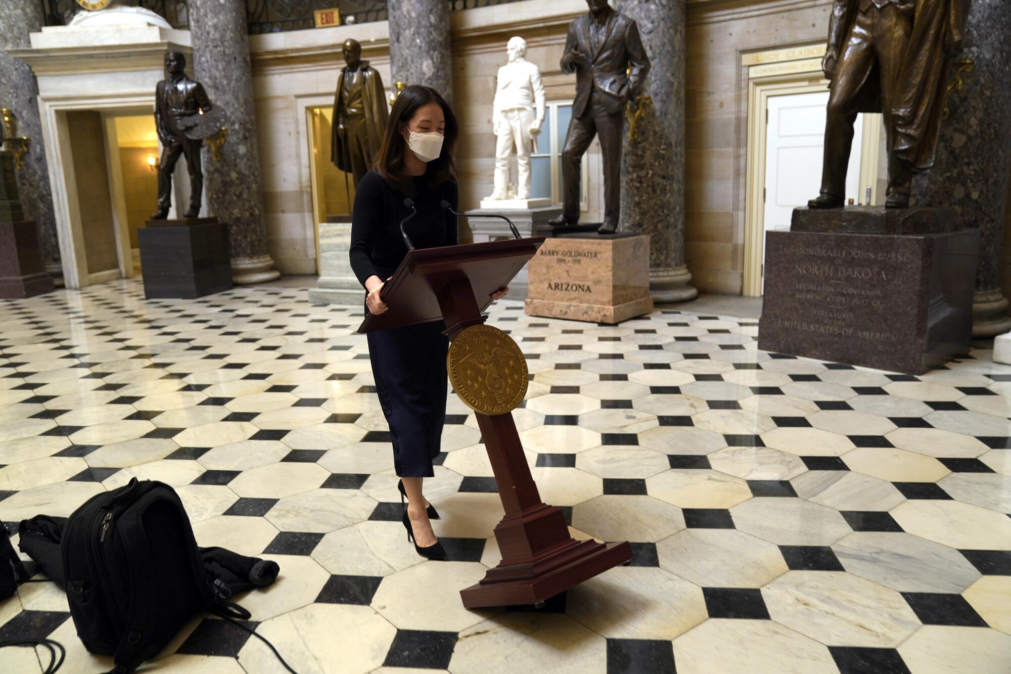 A woman tilts a lectern on a tiled floor. Statues are seen in the background. 