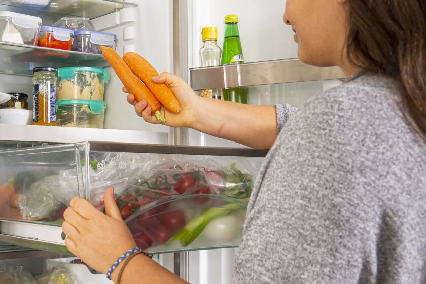 Woman grabbing carrots from the drawer fridge.