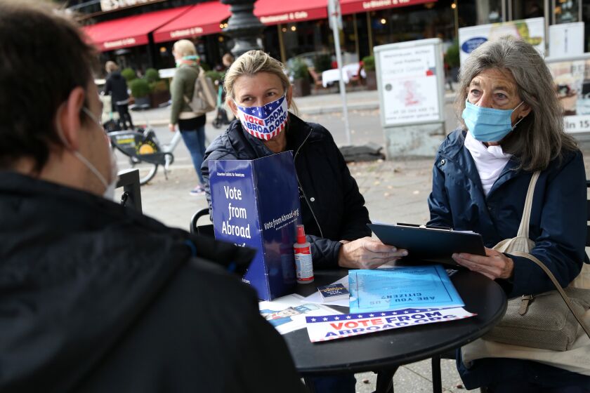 BERLIN, GERMANY - OCTOBER 10: Renee Johnsson of Democrats Abroad (C) and Florian Schiedhelm of Vote from Abroad (L) assist U.S. citizen Emily Schalk to register to vote absentee in the U.S. presidential elections to be held on November 3, at a Starbucks coffeeshop on October 10, 2020 in Berlin, Germany. Approximately 2.9 million Americans are eligible to vote from abroad, according to estimates from the Federal Voting Assistance Program. (Photo by Adam Berry/Getty Images)