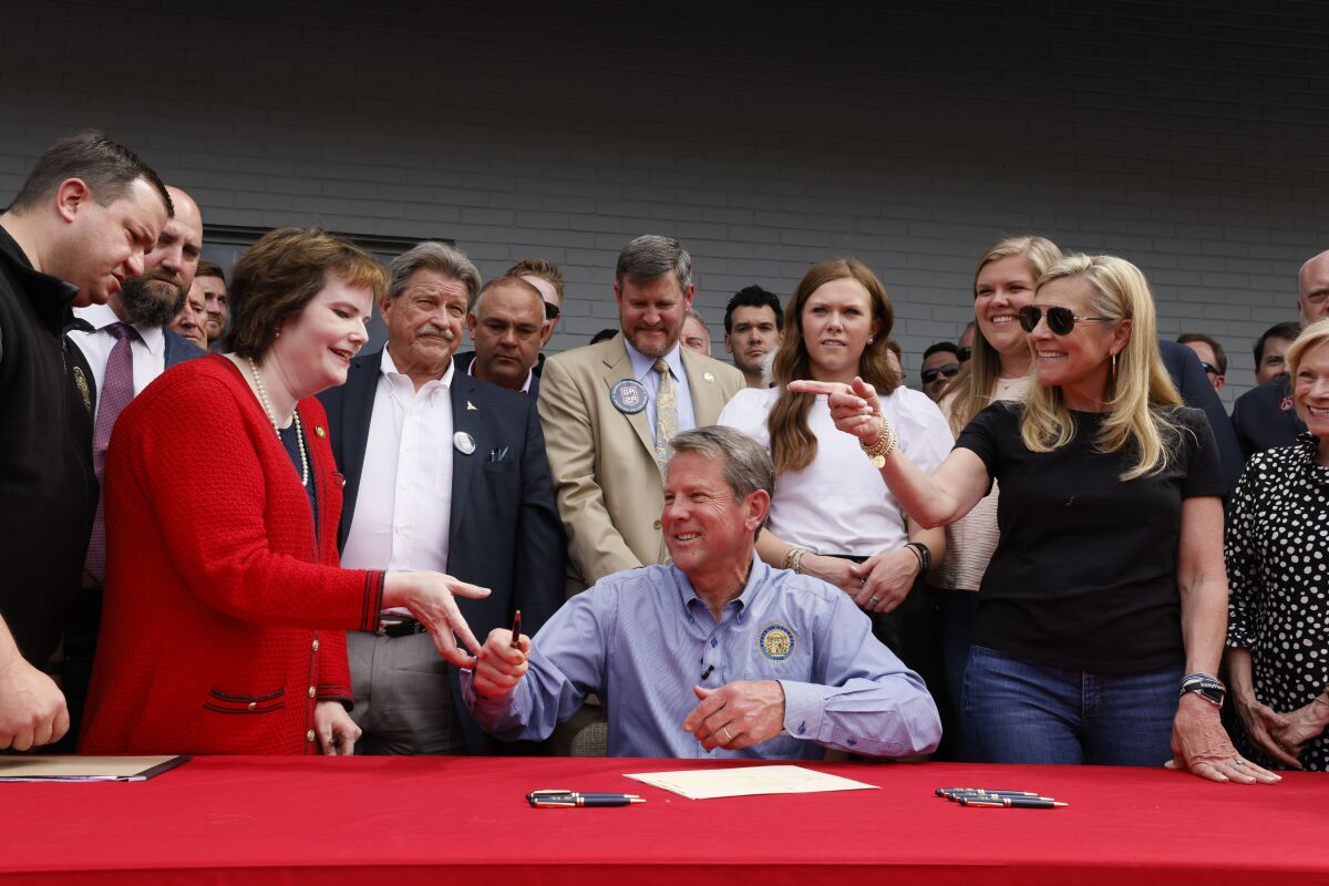 Gov. Brian Kemp hands a pen to Rep. Mandi Ballinger after he signed a bill which will allow permit less carry at a sporting goods store in Douglasville, Ga., Tuesday, April 12, 2022. SB 319 allows a "lawful weapons carrier" to carry a concealed handgun everywhere license holders currently are allowed. (Bob Andres/Atlanta Journal-Constitution via AP)