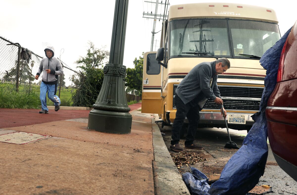 A man sweeping in front of an RV parked along a sidewalk