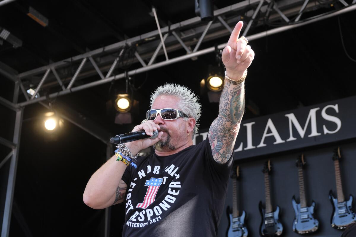 Guy Fieri speaks into a microphone and points.