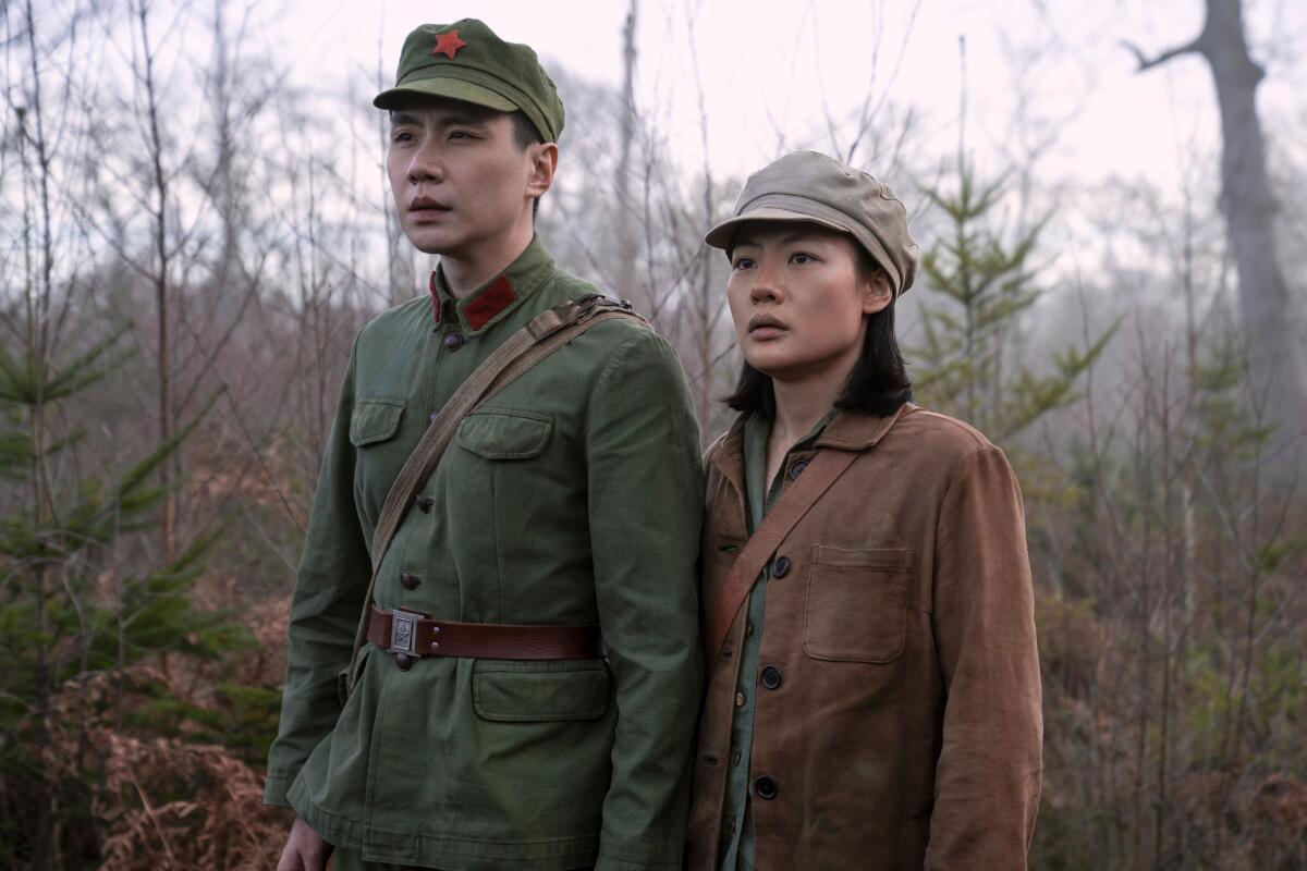 A man and a woman in uniforms stand in a forest.