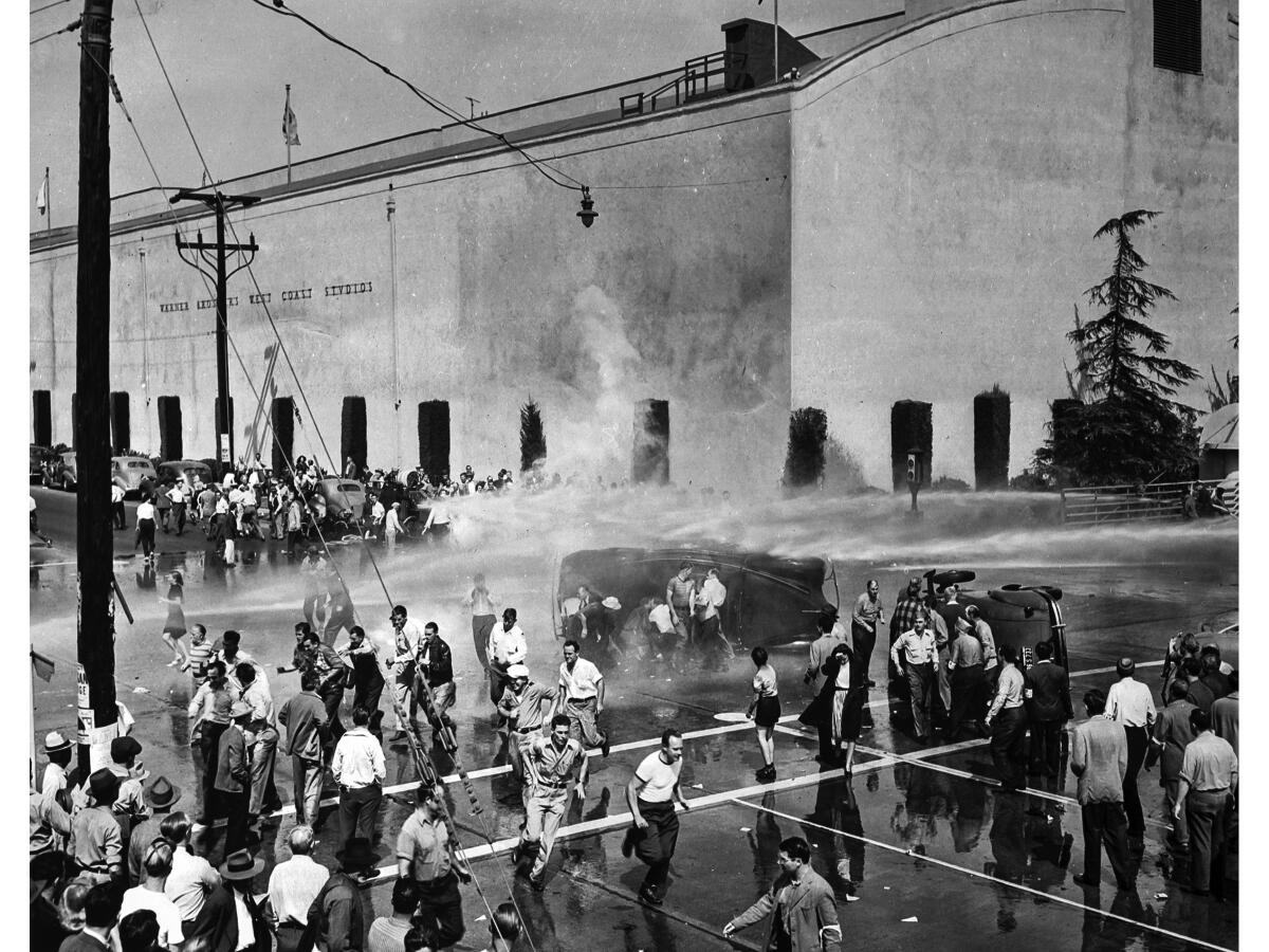 Oct. 5, 1945: Strikers outside Warner Bros. Studios in Burbank scatter and others take cover behind overturned cars as studio firefighters turn hoses on the strikers. 