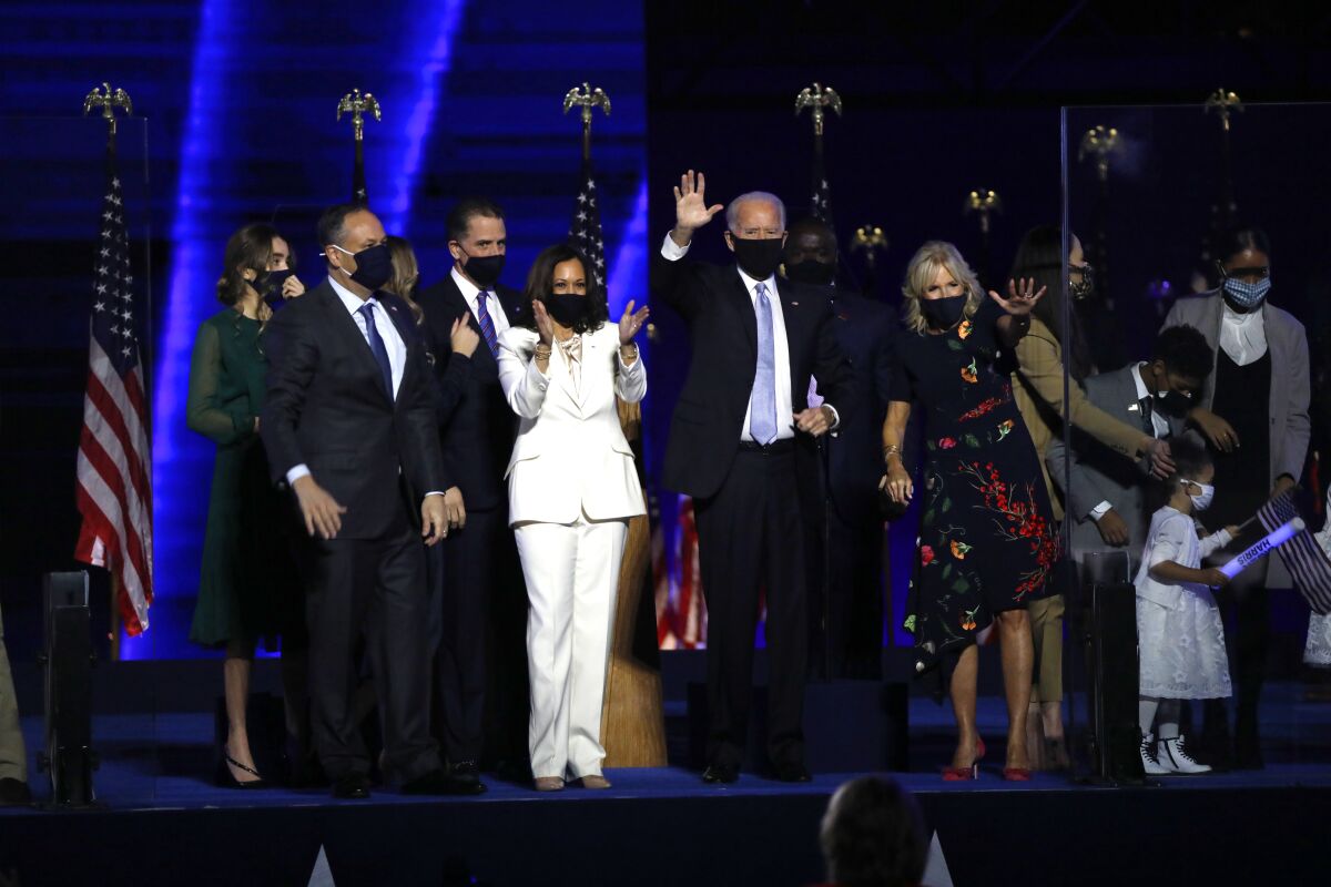 President-elect Joe Biden and Vice President-elect Kamala Harris wave to supporters from a stage with other people near them.