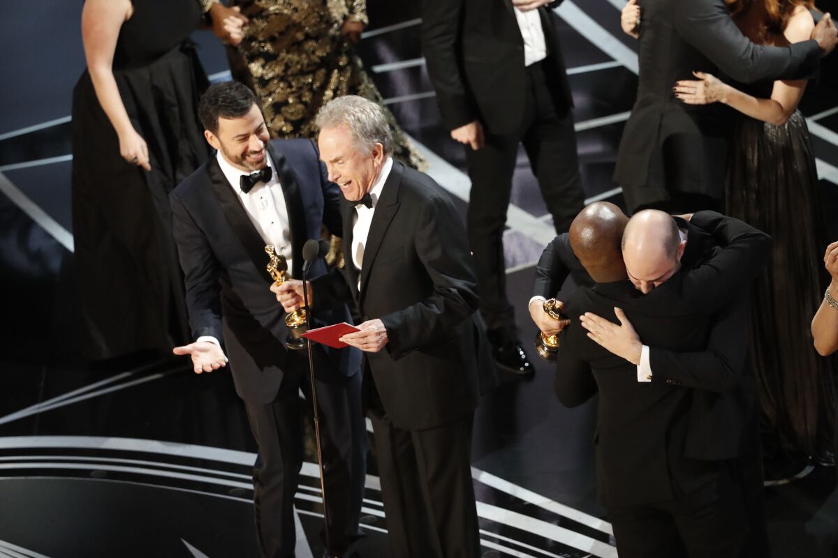 A man in a tux smiles at another man in a tux who is holding an Oscar 