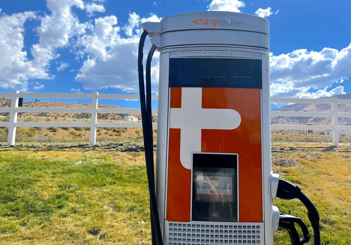 An EV charging station. In the background is a white fence and scrubby hills.