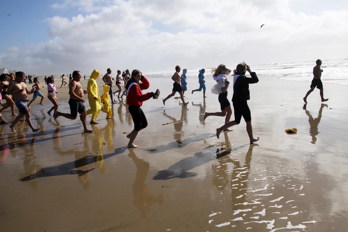 Hundreds of people, some wearing costumes, run into the chilly Pacific Ocean on Sunday for the annual Surf City Splash.