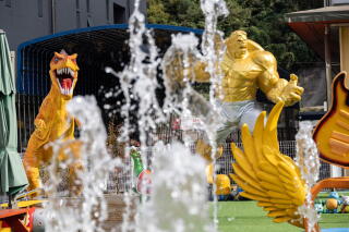 Streams of water rise near sculptures of a dinosaur and a muscled figure