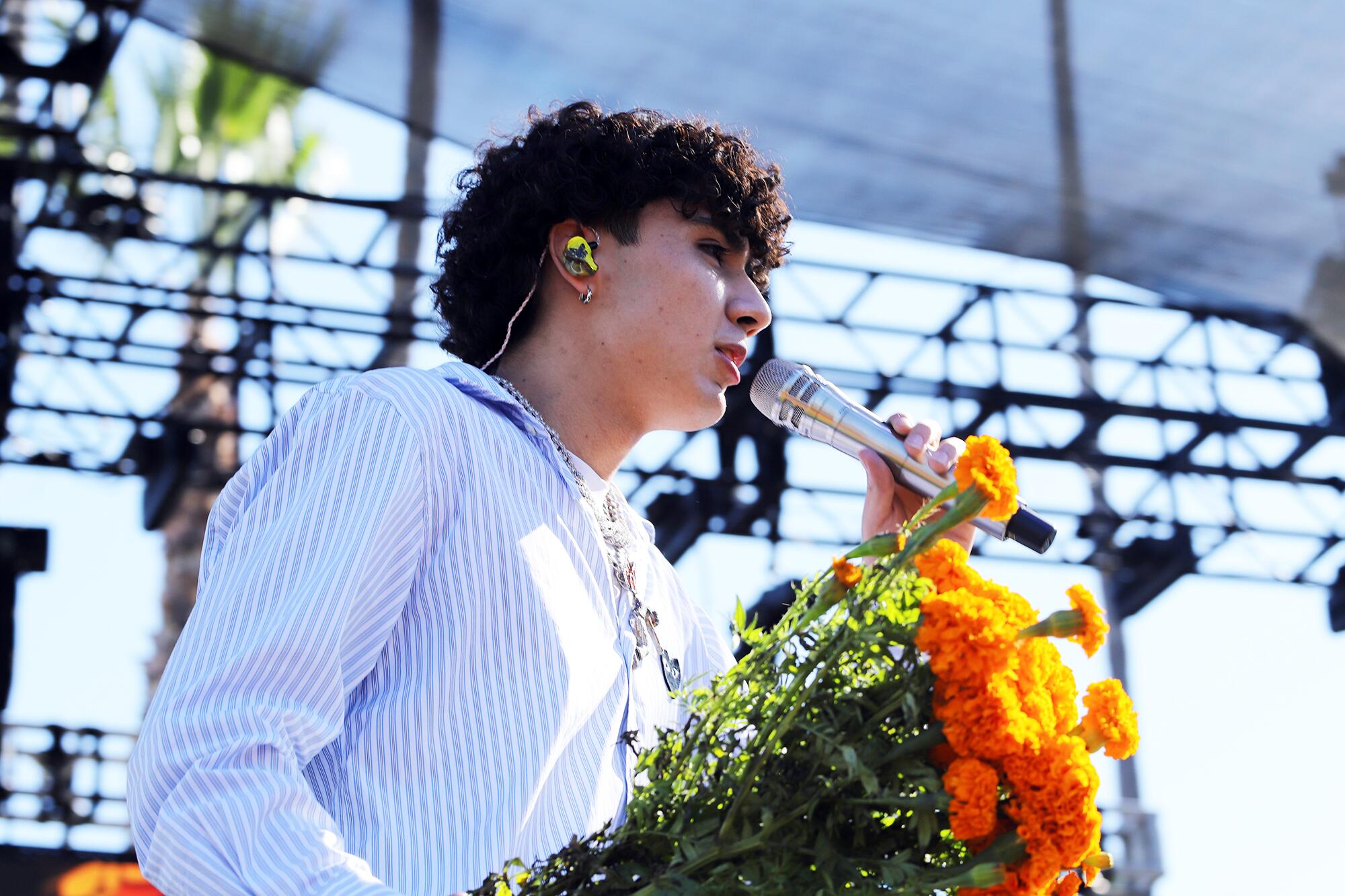 A man sings into a microphone while holding flowers