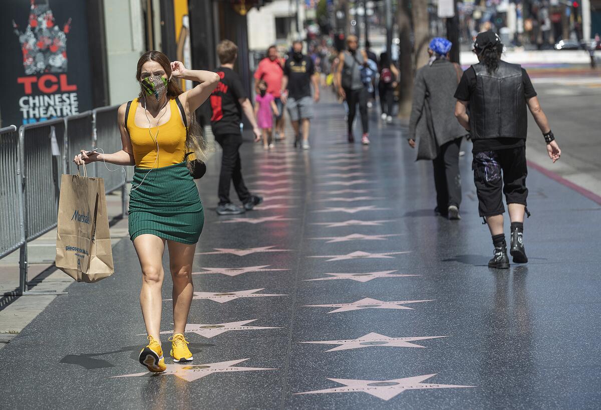 A pedestrian adjusts her face covering while walking along Hollywood Boulevard in Hollywood.
