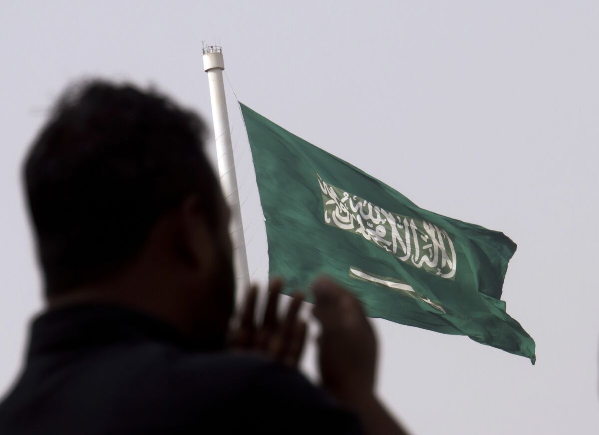 FILE - A man prays at an open air makeshift mosque in front of a giant Saudi Flag in Jiddah, Saudi Arabia, June 21, 2017. Saudi Arabia is inching towards changes that govern its national anthem and green flag, which is emblazoned with a sword and inscribed with Islam’s creed. State-owned media reported the kingdom’s un-elected consultative Shura Council voted in favor of changes late Monday, Jan. 31, 2022. (AP Photo/Amr Nabil, File)