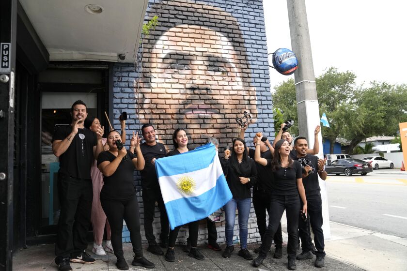 Personal del restaurante Fiorito porta una bandera de Argentina frente a un mural de Lionel Messi en Miami, el miércoles 7 de junio de 2023 (AP Foto/Lynne Sladky)