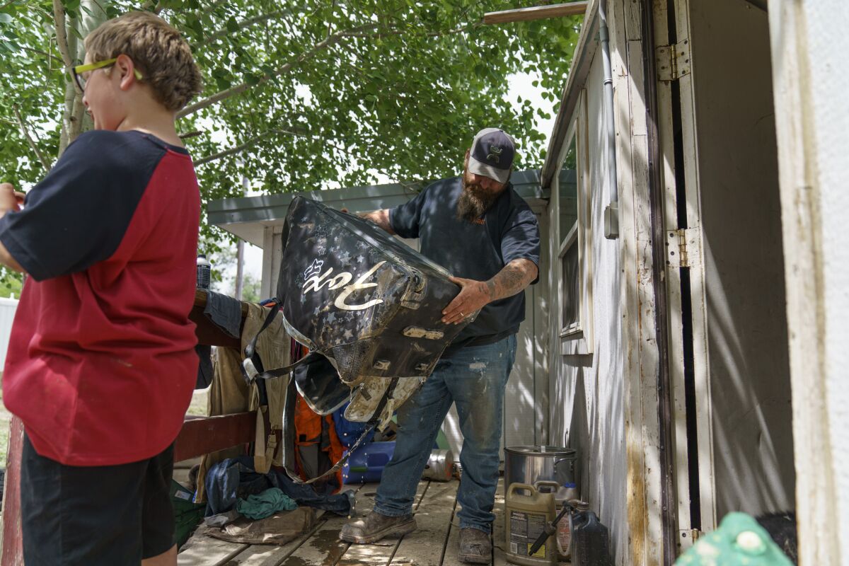 Matt Holmes, right, drains a suitcase while packing up belongings with his son, Gavin, 9, as the family is forced to leave their home left damaged by severe flooding in Fromberg, Mont., Friday, June 17, 2022. (AP Photo/David Goldman)