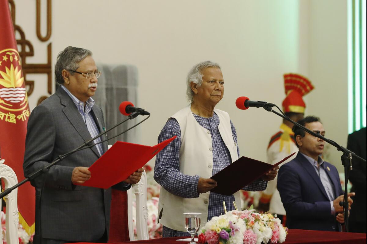 Two men hold folders as they stand in front of microphones.