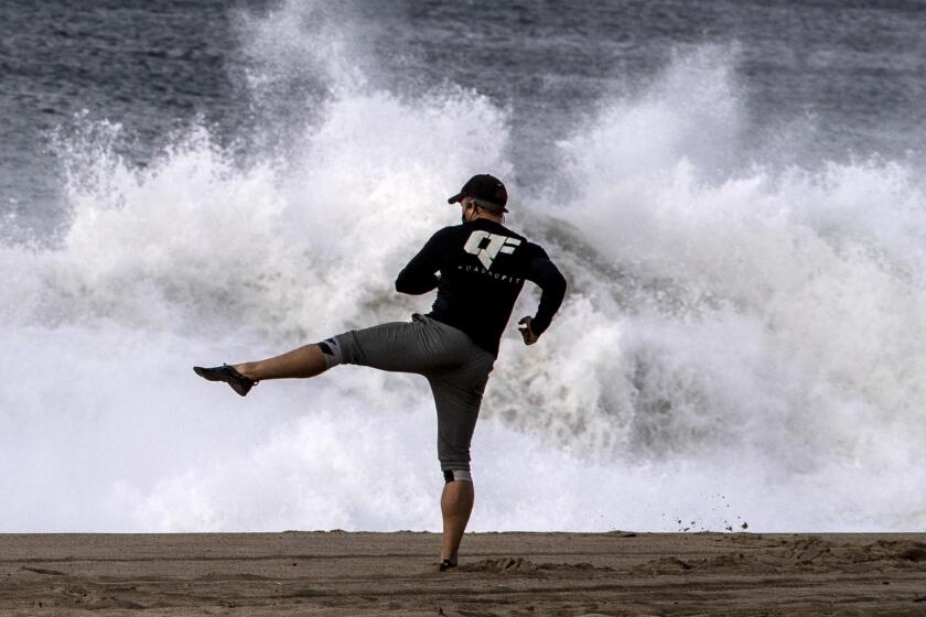 MALIBU, CA - DECEMBER 08: Kevin Cannon of Canoga Park works out on the beach as winds push sea spray from large waves crashing on the shore at Point Dume Tuesday, Dec. 8, 2020 in Malibu, CA. (Brian van der Brug / Los Angeles Times)