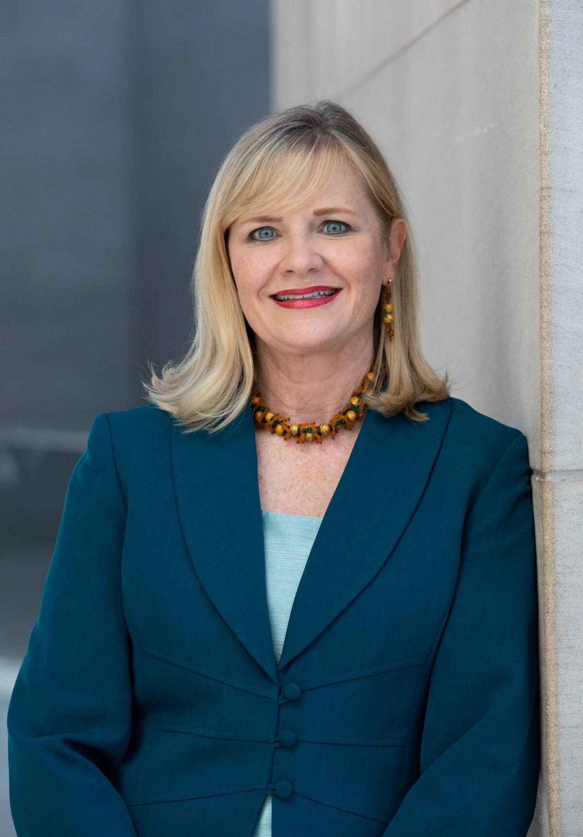 A smiling blond woman in a teal jacket.