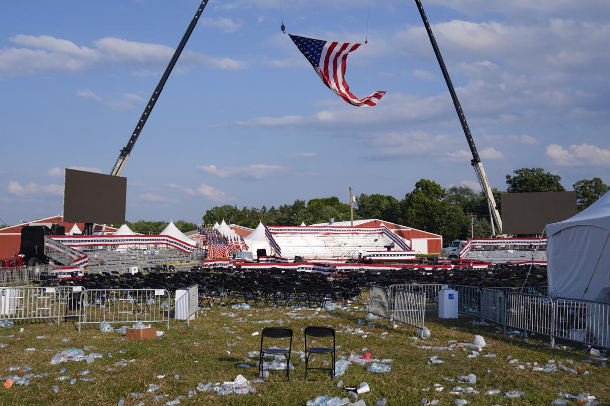 An American flag flutters over an empty fairgrounds filled with leftover tents, chairs, barricades and debris