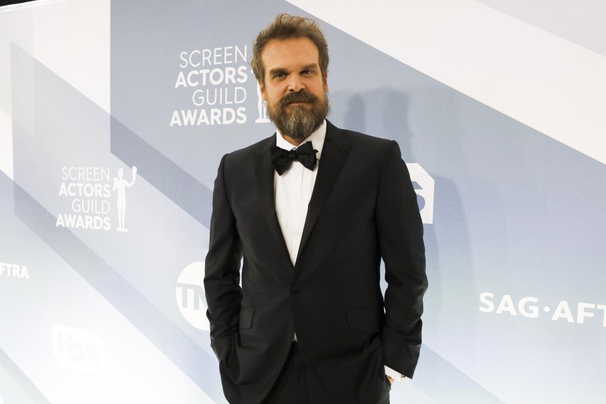 A bearded man wears a tuxedo and poses for pictures at a red carpet event