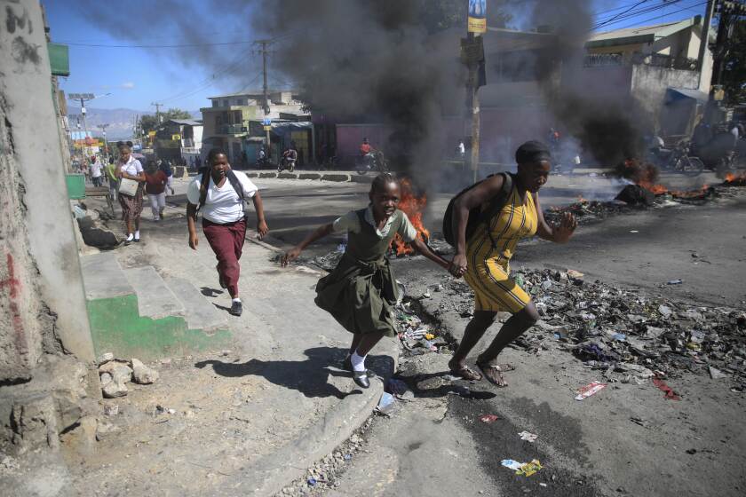 Archivo - Una mujer y su hija pasan corriendo frente a una barricada levantada por la policía en protesta por el mal gobierno policial en Puerto Príncipe, Haití, el 26 de enero de 2023. Las casi 200 pandillas de Haití se han aprovechado del caos, luchando por el control. (AP Foto/Odelyn Joseph, Archivo)