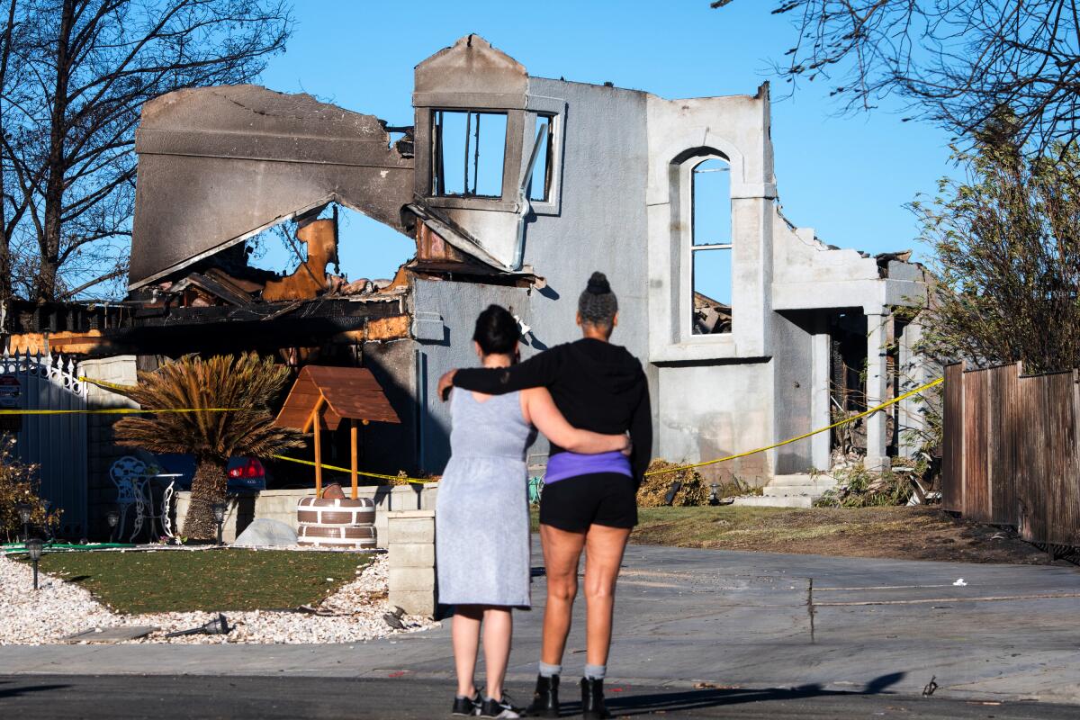 Two people look at a neighbor's burned home. 