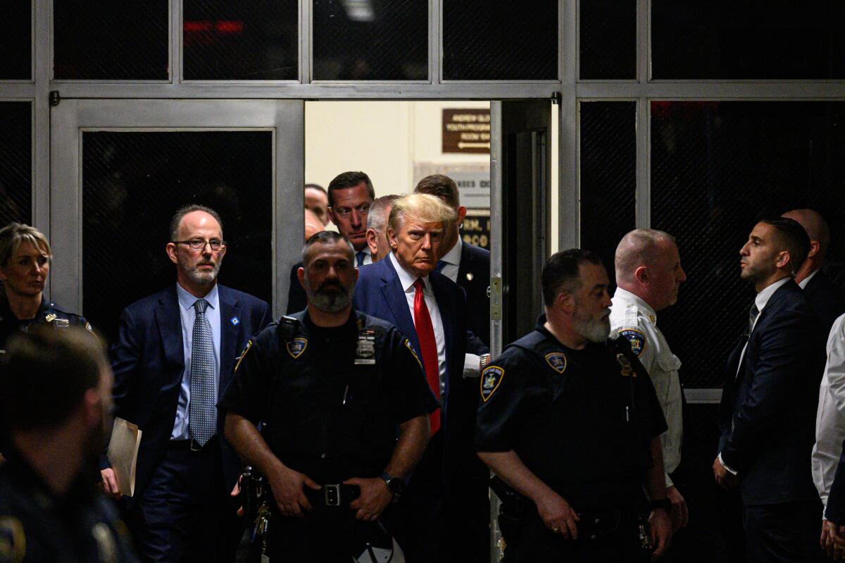 Donald Trump appears in a doorway surrounded by court security, personnel and lawyers.