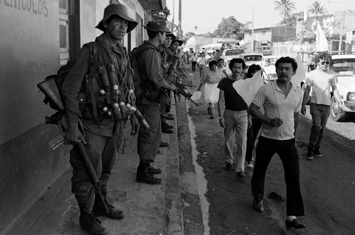 Salvadorans walk past troops in El Salvador in 1989.