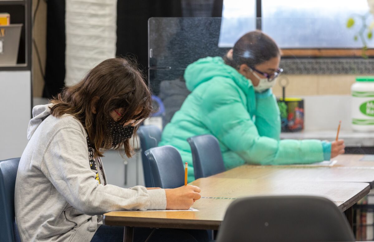 McAuliffe Elementary fifth-graders Mercedes Hopkins and Maia Ramirez are separated by plexiglass during class