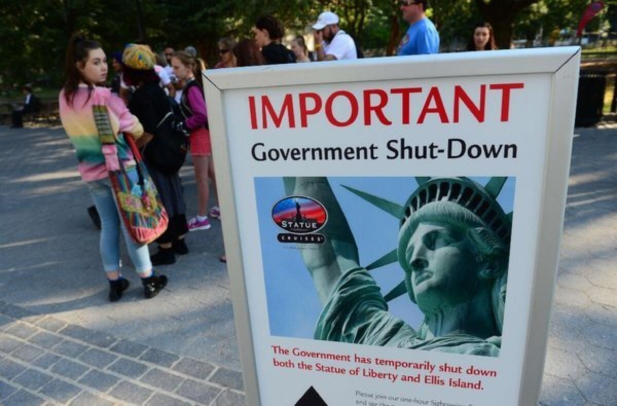 Tourists walk by a sign announcing that the Statue of Liberty is closed due to a federal government shutdown.