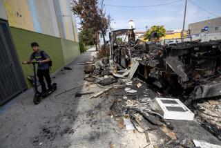 Los Angeles, CA - July 30: A man on a scooter rolls past a burned out RV sitting on the 1300 block of W. Washington Blvd. on Sunday, July 30, 2023 in Los Angeles, CA. The RV has been there for three weeks. (Brian van der Brug / Los Angeles Times)