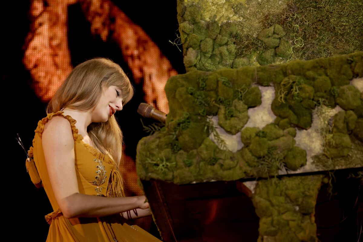 A woman plays the piano on a stage covered in grass
