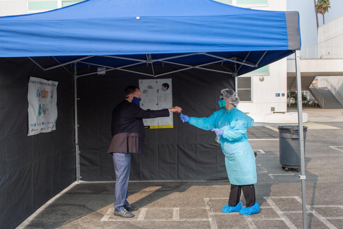 A health worker in blue protective gear hands a test kit to Superintendent Austin Beutner