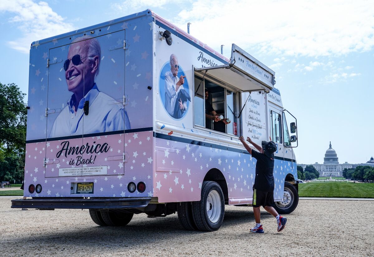 A child reaches for an ice cream cup afrom an ice cream truck with President Biden's picture