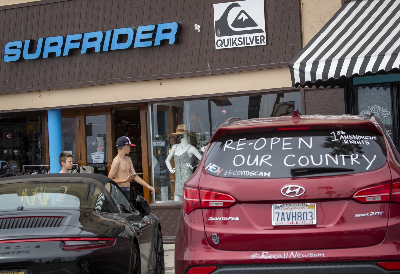 NEWPORT BEACH, CA -- TUESDAY, APRIL 28, 2020: A motorist makes a statement on their car as pedestrians walk past a mannequin wearing a protective mask in a store window display near the pier in Newport Beach, CA, on April 28, 2020. Newport Beach City Council members hold a special meeting to discuss closing the city's beaches for the next few weekends following Gov. Gavin Newsom's criticism of the large crowds and lack of social distancing.(Allen J. Schaben / Los Angeles Times)