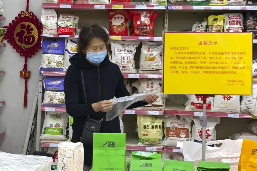A woman wearing a mask shops near a sign which calls for shoppers to be vigilant against the coronavirus rebounding and not to listen to rumors and to avoid stockpiling at a supermarket in Beijing, China, Wednesday, Nov. 3, 2021. A recent seemingly innocuous government recommendation for Chinese people to store necessities for an emergency quickly sparked scattered instances of panic-buying and online speculation of imminent war with Taiwan. (AP Photo/Ng Han Guan)