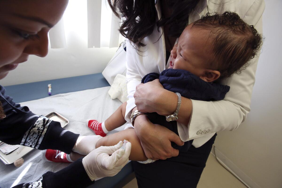 Medical assistant Daisi Minor, left, gives a measles-mumps-rubella vaccine to Kristian Richard, 1, being held by his mother, Natasha, at the Medical Arts Pediatric Med Group on Wilshire Boulevard in Los Angeles this month.