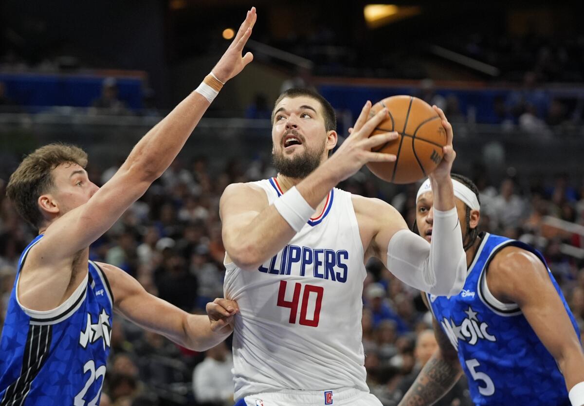 Clippers center Ivica Zubac takes a shot under the basket against Orlando Magic's Franz Wagner and Paolo Banchero