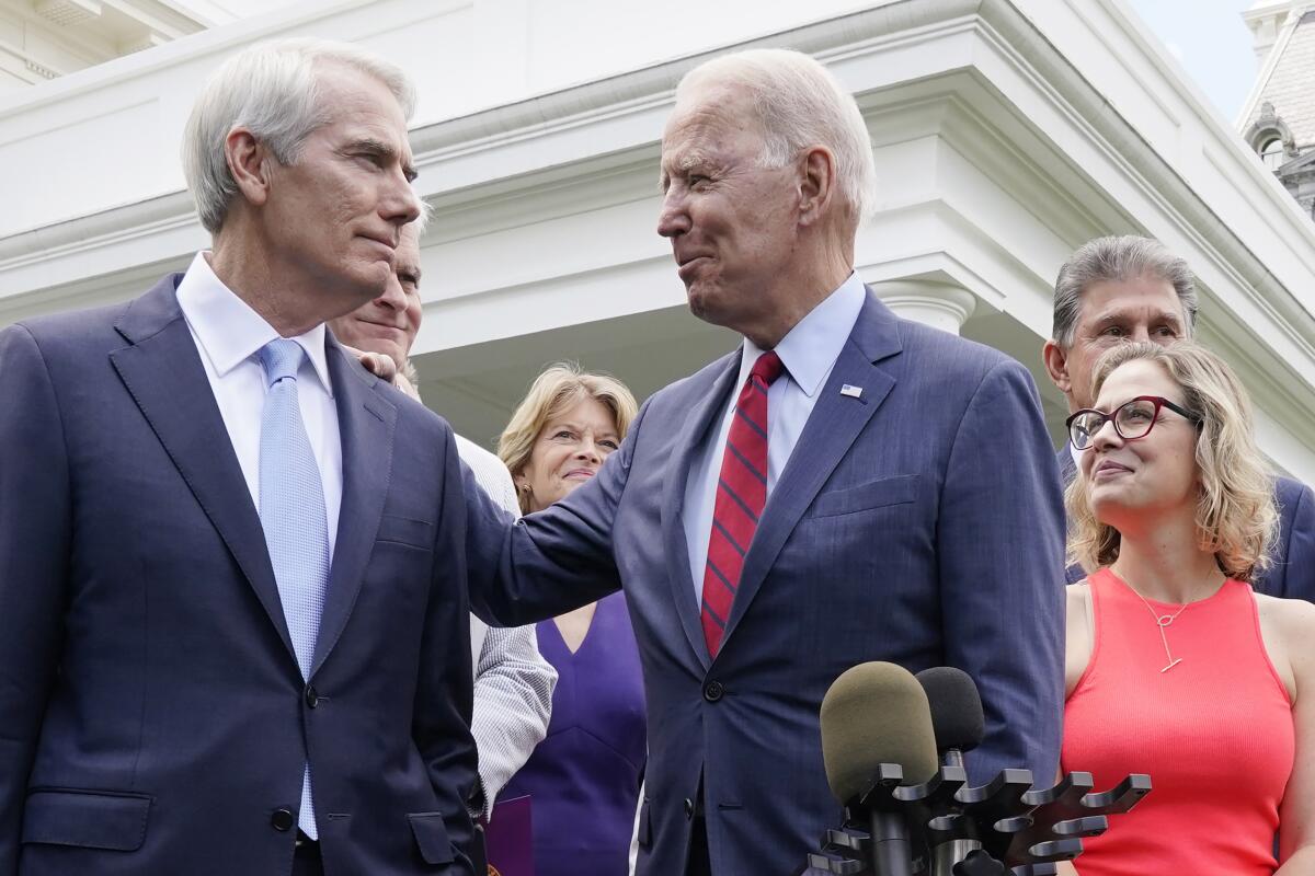 Amid a crowd and in front of microphones, Joe Biden pats Rob Portman on the shoulder.