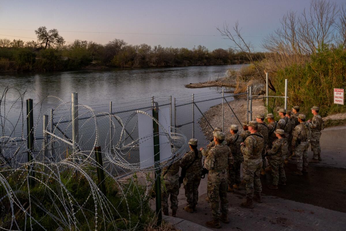 Several soldiers standing guard behind a fence and razor-wire on a riverbank