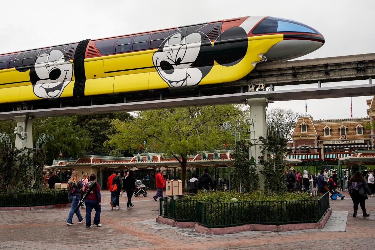 The Disneyland Monorail passes by as people walk toward the park entrance in March 2020.