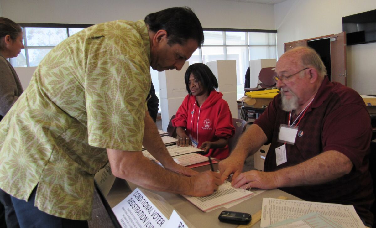 Lemon Grove resident Tomas Martinez signs his name before voting in Tuesday's election with election volunteers Terry Hoopes (right) and Jackie Spicer (center) helping with paperwork at the Lemon Grove Library.