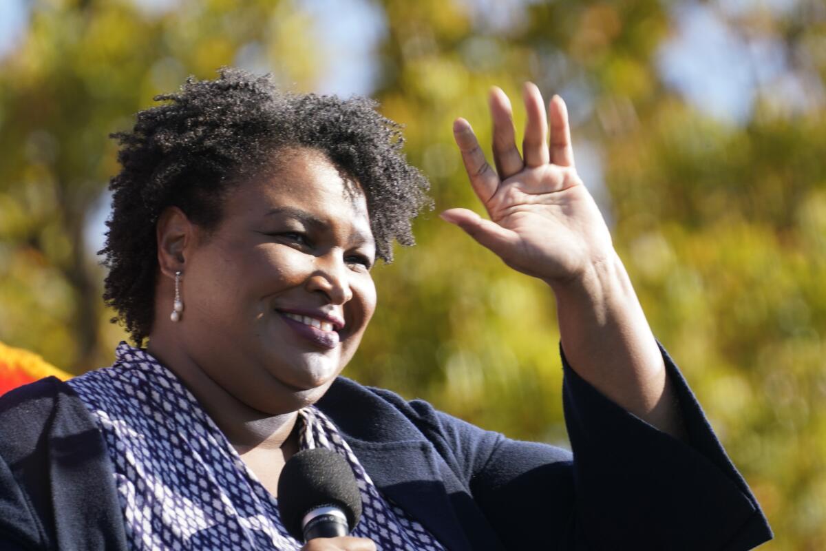 Stacey Abrams holds a microphone and waves