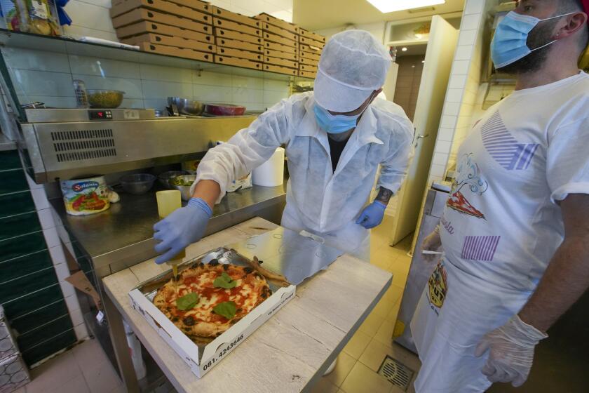 Olive oil is put on a pizza ready to be home delivered, at the Caputo pizzeria in Naples, Italy, Monday, April 27, 2020. Region Campania allowed cafes and pizzerias to reopen for delivery Monday, after a long precautionary closure due to the coronavirus outbreak. (AP Photo/Andrew Medichini)