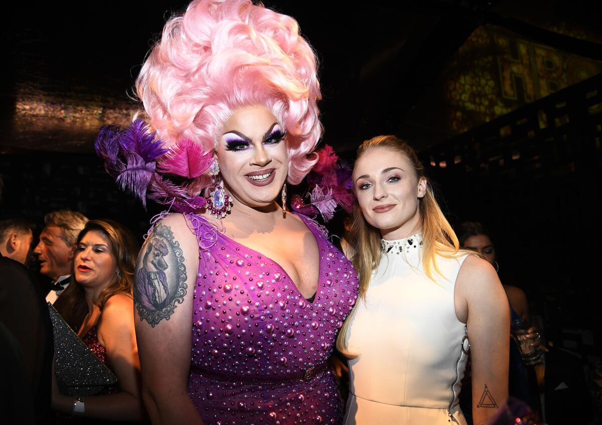 Drag queen Nina West wears a purple gown and cotton candy pink wig next to actress Sophie Turner, dressed in white.