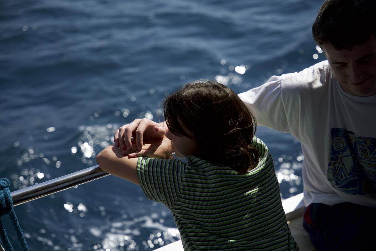 Two boys lean over a boat railing toward the sparkling water.