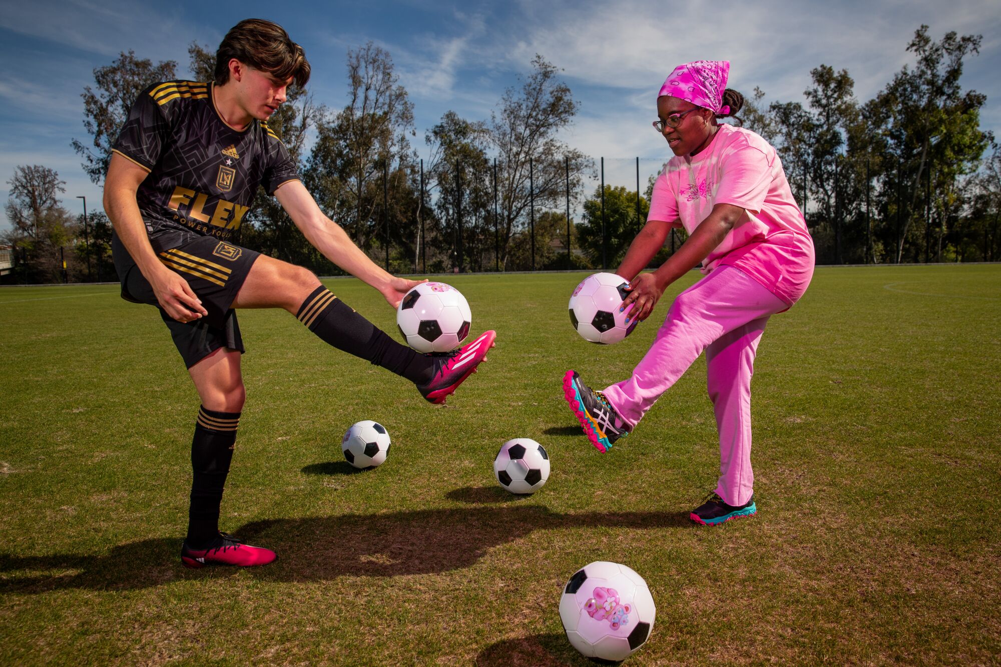 A man in black shorts and a top and a woman in pink hold soccer balls.