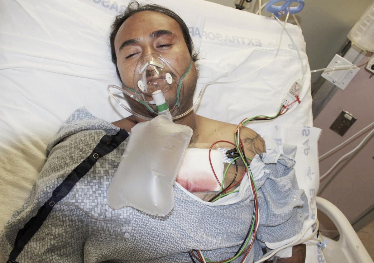A man with an oxygen mask and blood-soaked gauze pad on his chest lies in a hospital bed.