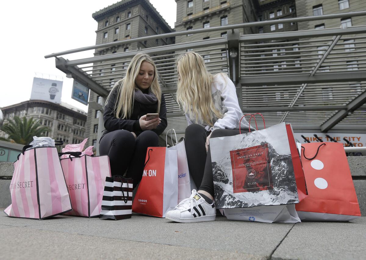 Shoppers sit with bags at Union Square in San Francisco on Nov. 25. U.S. consumers boosted their spending again in October, while their incomes increased at the fastest clip in six months, according to the Commerce Department.