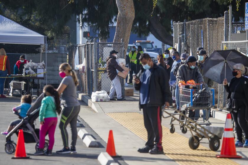 SOUTH GATE, CA - NOVEMBER 25: A man carries home a box of free meals, center, after waiting in a long line of people walking in, which was in addition to a line of cars that wrapped around several streets, picking up their free meals as the Los Angeles Unified School District, the nation's second-largest school district, distributes 1.5 million meals the day before Thanksgiving, helping families in need bridge the long weekend at South Gate High School on Wednesday, Nov. 25, 2020 in South Gate, CA. District leaders, including Supt. Austin Beutner, attended, helped distribute food and had a meal with recipients. (Allen J. Schaben / Los Angeles Times)