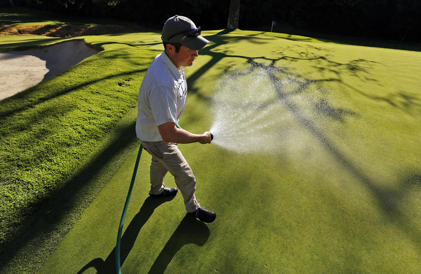 Jordan Gilmore, assistant superintendent at Riviera Country Club adds water by hand to the 12th green in the shadow of a sycamore tree known as "Bogart's tree" as the course prepares to host the Northern Trust Open.